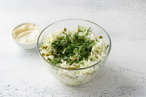 Glass bowl of cabbage salad with cucumbers, green peas, chopped herbs and mayonnaise dressing. Cooking delicious homemade salad. Step-by-step instruction. Step 3