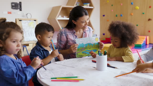 Cheerful teacher giving instructions to her diverse kindergarten class during art class