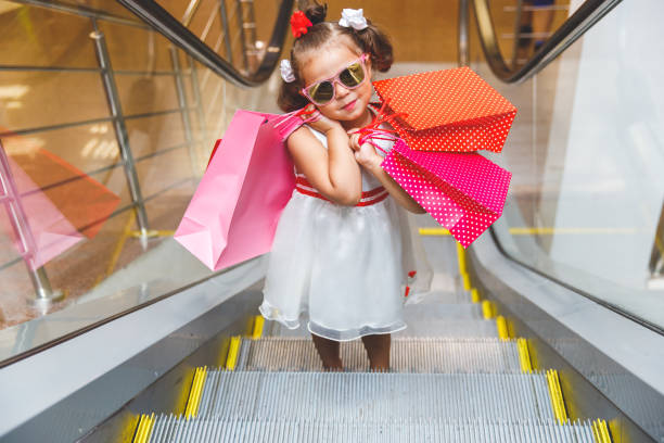 menina de óculos escuros na escada rolante no shopping com compras - escalator child shopping mall little girls - fotografias e filmes do acervo