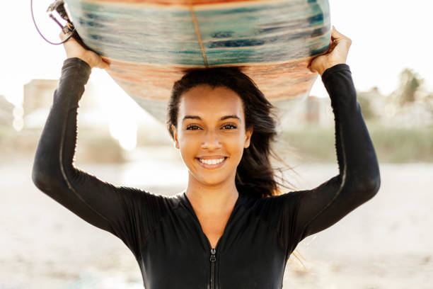 retrato de una joven surfista en la playa sosteniendo su tabla de surf - bikini surfboard women surfing fotografías e imágenes de stock