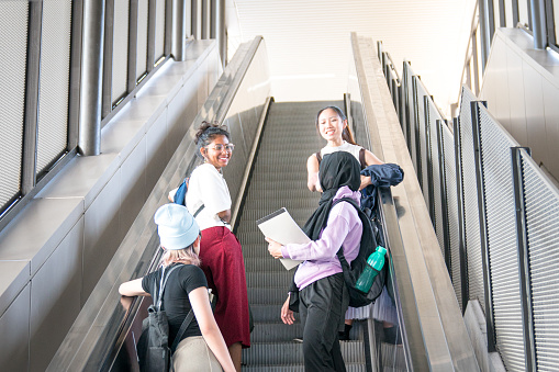 Group of happy young female students going up the escalator. Back to college concept.
