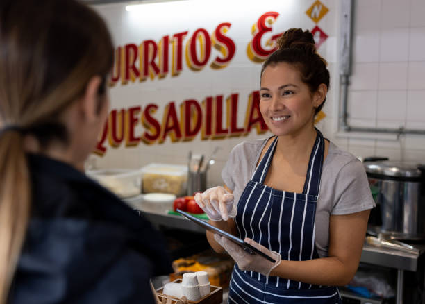 Woman working at a restaurant and using a tablet to take the customerâs order Latin American woman working at a street food restaurant and using a tablet to take the customerâs order - food service concepts point of sale tablet stock pictures, royalty-free photos & images