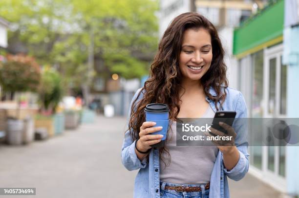 Happy Woman Drinking A Cup Of Coffee On The Move While Texting On Her Phone Stock Photo - Download Image Now
