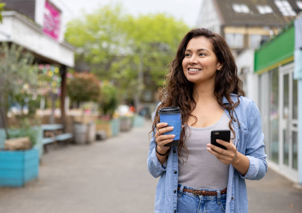istock Happy woman drinking a cup of coffee on the move while using her phone 1405734698