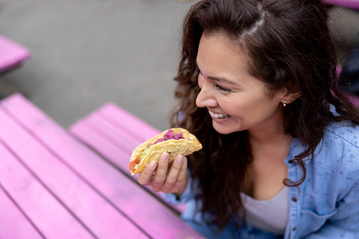 Happy Latin American woman eating tacos at an outdoor Mexican restaurant â street food concepts