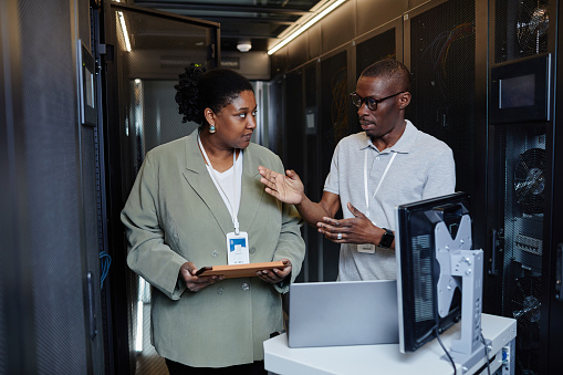 Waist up portrait of two IT engineers using laptop in server room while setting up network