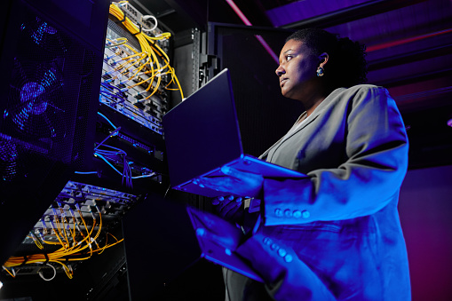 Low angle portrait of female network engineer setting up servers in data center lit by neon