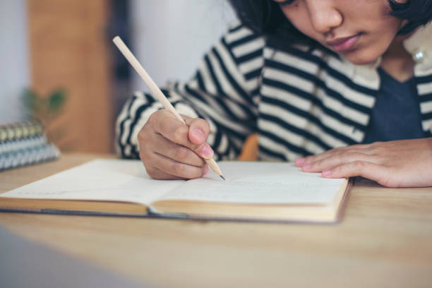 istock Asian elementary Children Writing Letter on diary book. Kid learn and work, read book, girl work at home. Cute Child doing and study homework. Little Child happy and smile. Education concept. 1405742470