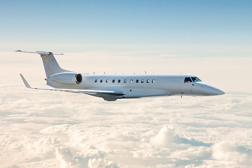 White business jet flies in the air above the clouds