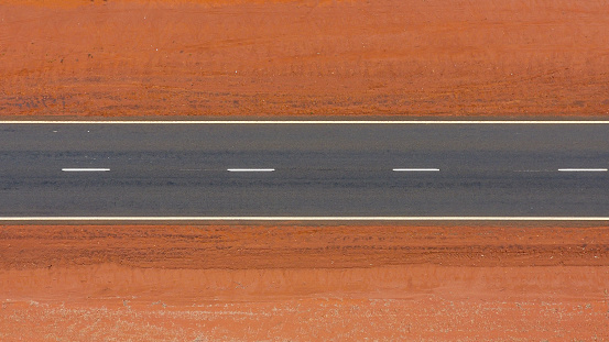 Photo taken from a drone of a 2 lane highway in the middle of Queensland, Australia. Road is empty and very straight surrounded by red dirt.