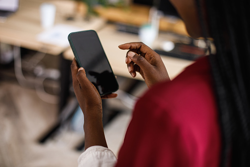 Close up shot of unrecognizable businesswoman holding smart phone, scrolling through her contacts when making a call.