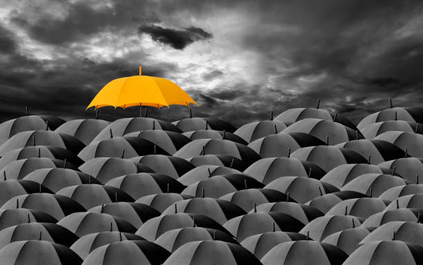 yellow umbrella surrounded by many black umbrellas against dark cloudy sky - protection insurance dark rain imagens e fotografias de stock