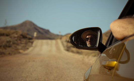 Adult man in sunglasses on side view mirror of car on dirt road