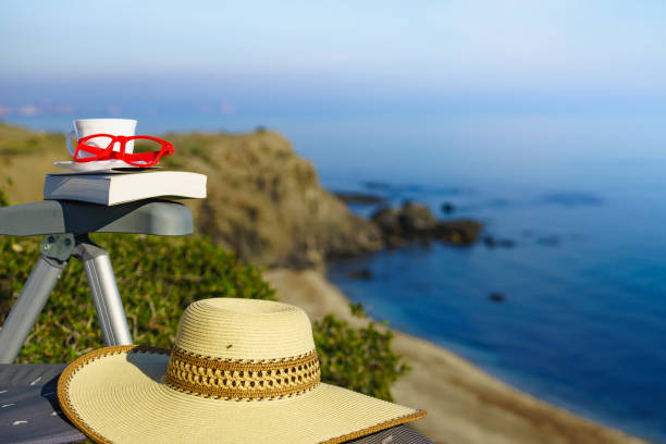 Spiritual healing, psyche silence. Coffee cup, book and red glasses against coast. Reading on vacation. Relaxation on holidays. Mental health break.