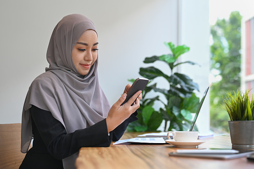 Muslim businesswoman wearing headscarf sitting front of laptop computer and sig mobile phone.