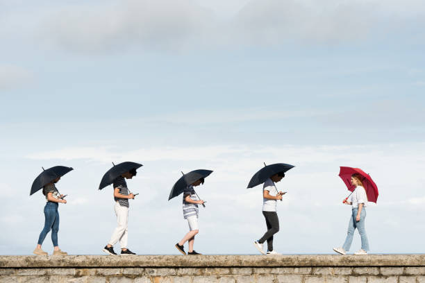 giovane donna che cammina in direzione opposta alla folla - standing out from the crowd individuality umbrella contrasts foto e immagini stock