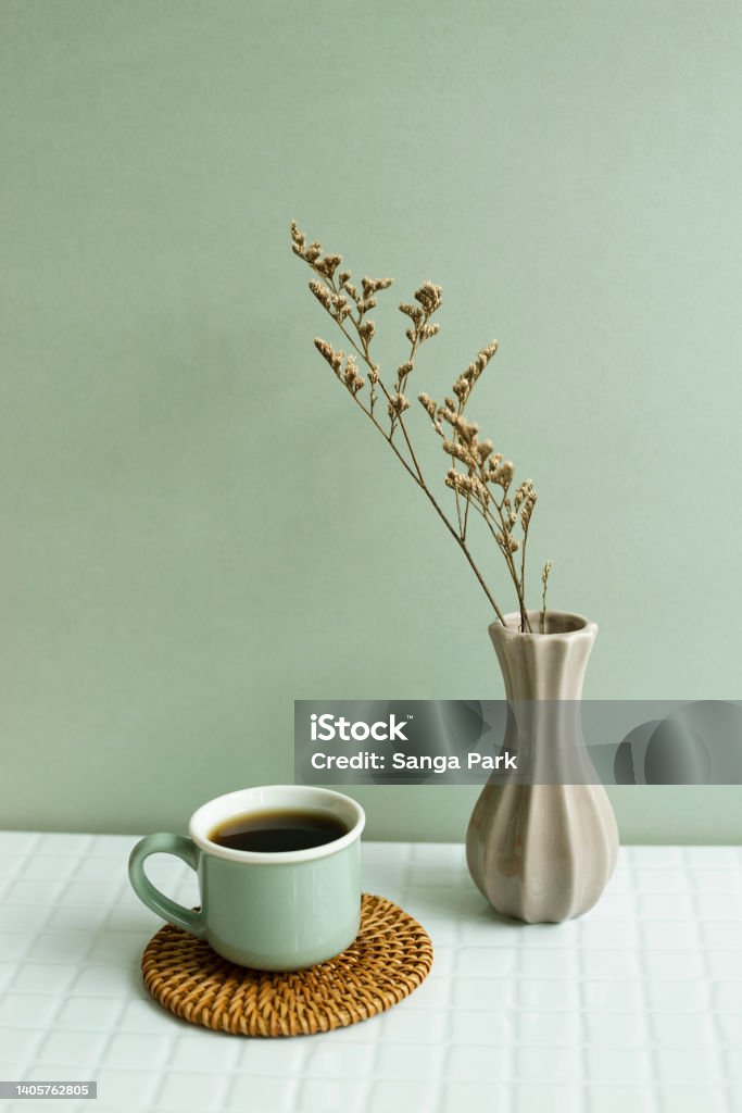 Cup of coffee and dry flowers on white table. khaki green wall background Coaster Stock Photo