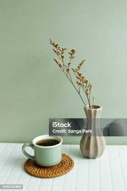 Cup Of Coffee And Dry Flowers On White Table Khaki Green Wall Background Stock Photo - Download Image Now