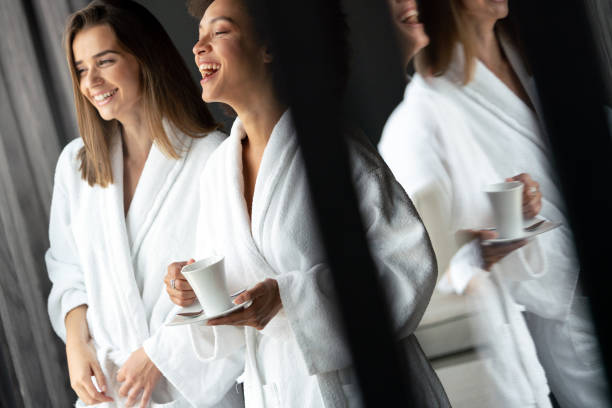 mujeres relajadas y bebiendo té en batas durante el fin de semana de bienestar - bathrobe women cup towel fotografías e imágenes de stock