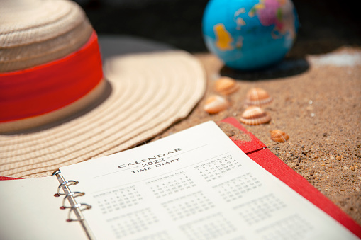 Planner notebook, sun hat and globe on sand beach close up. Summer Vacation travel planning concept.