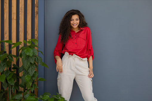 Young woman in red shirt standing against grey and wooden wall.
