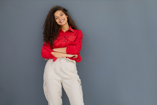 Young woman in red shirt standing against grey wall.