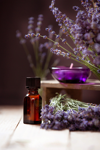 Herbal oil, candle and lavender flowers still-life on wooden background, selective focus