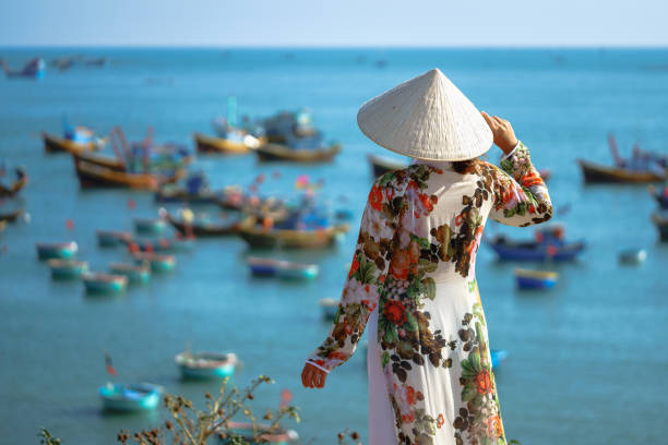 Vietnamese lady with Ao Dai Vietnam traditional dress Vietnamese lady with Ao Dai Vietnam traditional dress and conical hat wait at the harbor, Fishing Harbour Mui Ne Vietnam mui ne bay photos stock pictures, royalty-free photos & images