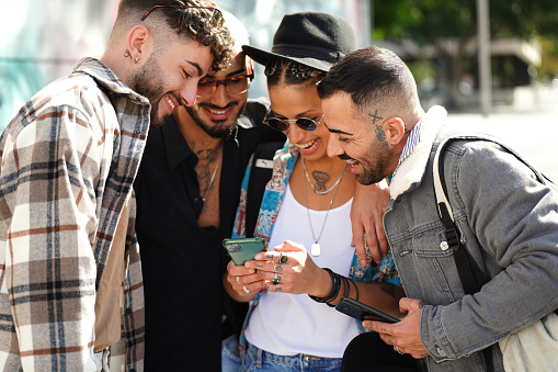 Happy group of friends watching social media on screen mobile phone, laughing. Young people using smartphone, having fun together in the city. Tourists. Traveler.