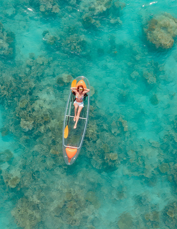 Beautiful woman enjoying her vacation on glass bottom kayak in tropical ocean
