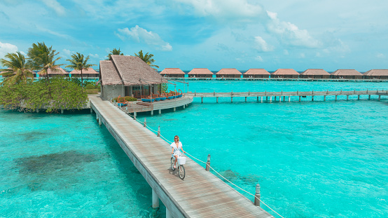 Young woman with bicycle on wooden pier in the Maldives