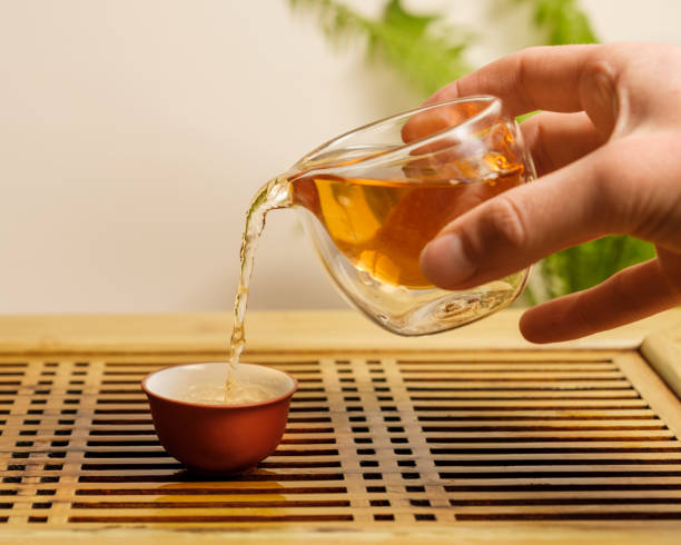 la mano del hombre vierte té chino de un pequeño chahai de vidrio en una taza de cerámica. - tea cup cup china saucer fotografías e imágenes de stock