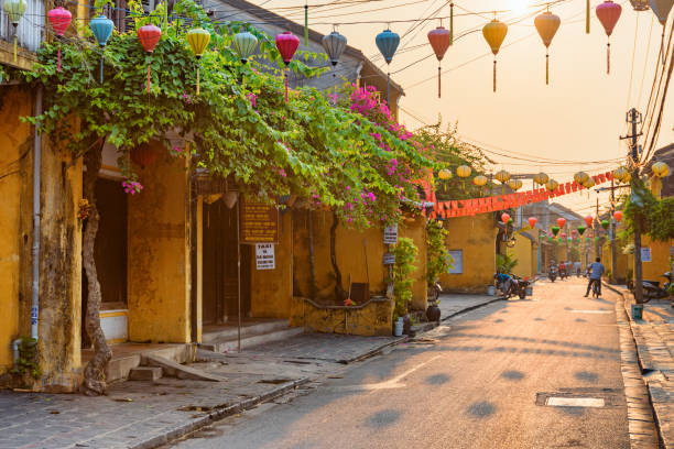 Scenic cozy street decorated with silk lanterns, Vietnam Hoi An (Hoian), Vietnam - April 12, 2018: Scenic cozy street decorated with colorful silk lanterns at sunrise. Awesome traditional old yellow houses of Hoi An Ancient Town. hoi an stock pictures, royalty-free photos & images