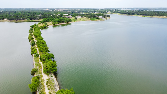 Top view lush green hiking trail lead to the lakeside neighborhood with upscale two story house in Lakewood Village, Texas, America. Long straight lakeside unpaved road path to horizontal line