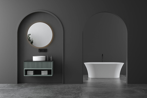 Stylish bathroom with gray and dark walls, concrete floor, comfortable bathtub and white sink with mirror. Minimalist design of modern dark bathroom. 3d rendering