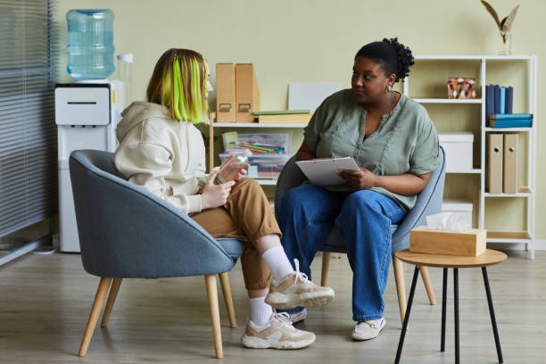 Woman social worker talking to teenage girl at office African female social worker talking to difficult teenage girl while they sitting on armchairs at office community outreach stock pictures, royalty-free photos & images