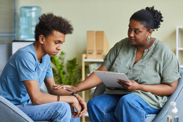 Psychologist working with teenage boy at office African psychologist supporting depressed teenage boy feeling guilty about behavior during therapy at office mental health professional stock pictures, royalty-free photos & images