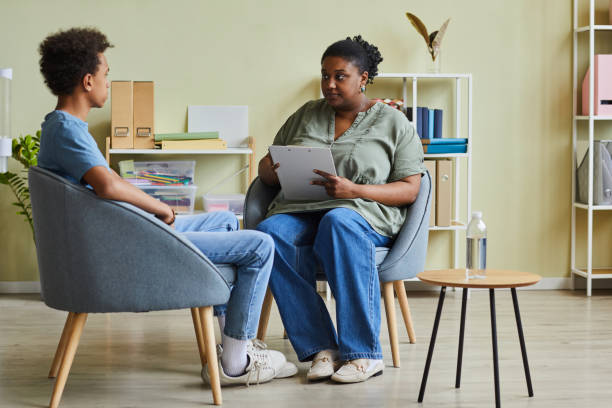 School psychologist talking to difficult teenager African school psychologist talking to difficult teenage boy during session while they sitting on armchairs at office community outreach stock pictures, royalty-free photos & images