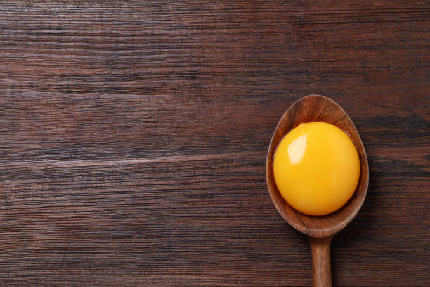 istock Spoon with raw egg yolk on wooden table, top view. Space for text 1405781135