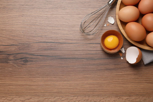 istock Chicken eggs, bowl with raw yolk and whisk on wooden table, flat lay. Space for text 1405781276