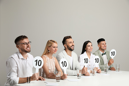 Panel of judges holding signs with highest score at table on beige background