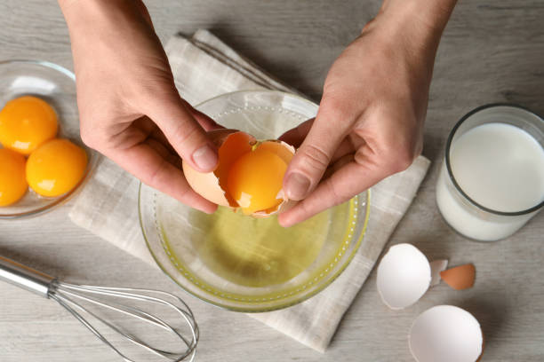 mujer separando la yema de huevo de la clara sobre el tazón de vidrio en una mesa de madera clara, vista superior - eggs fotografías e imágenes de stock