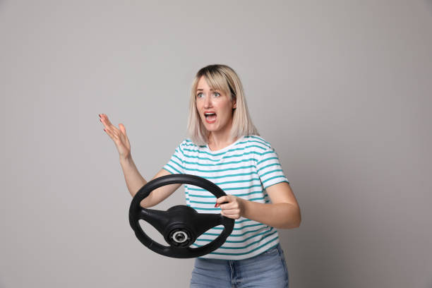 istock Emotional woman with steering wheel on grey background 1405783236