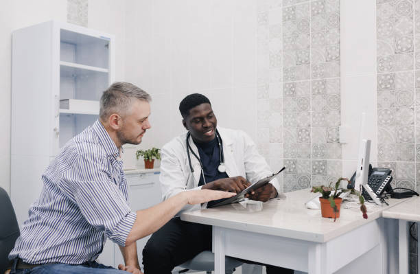 the patient and the doctor carefully study the results of the examination sitting at the table in the medical center. - medical exam doctor patient adult imagens e fotografias de stock