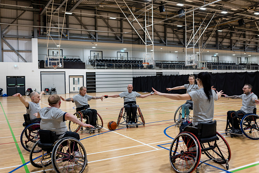 Team of wheelchair users playing basketball in the North East of England. They are practising in a circle, stretching and warming up with their arms outstretched.