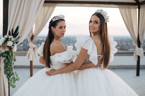 Two beautiful brides posing in sunset on terrace. Wedding dresses, friends and gorgeus decoration.