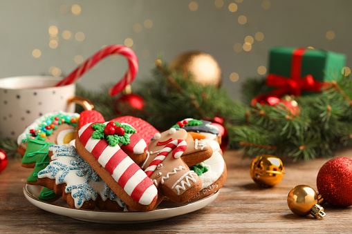 Stock photo showing close-up view of a snowy clearing, conifer forest scene. A homemade, gingerbread house decorated with white royal icing surrounded by model fir trees on white, icing sugar snow against a snowy blue background.