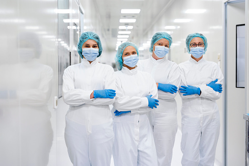 Four female employees in pharmaceutical industry seen in fully protective equipment in the hallway of the production plant of the company of drugs and nutritional supplements during their shift.