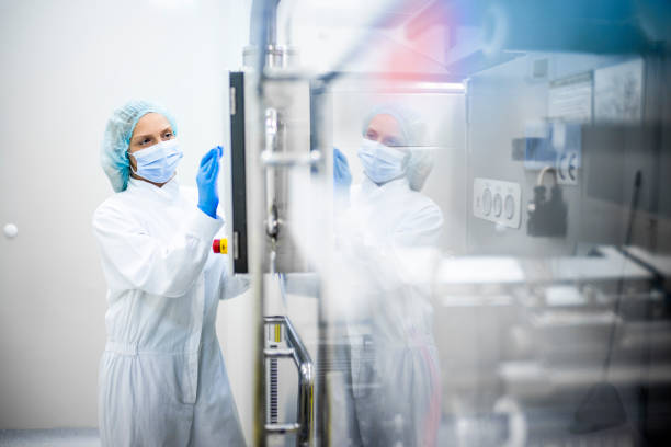 Pharmaceutical industry and drug manufacturing A woman wearing proper safety clothes seen taping on the screen of a big complex machine in pharmaceutical industry while her reflection is visible on the machine. biotechnology stock pictures, royalty-free photos & images