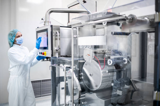 Drug manufacturing in pharmaceutical industry and its female employee seen taping on the screen of a machine stock photo